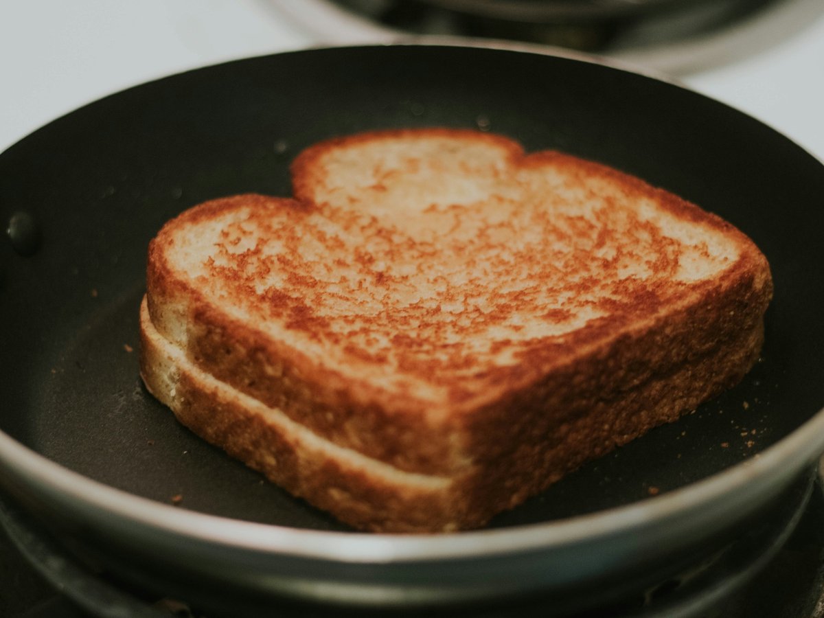 A thick, deep-gold grilled cheese sandwich sitting in a black frying pan on the stove