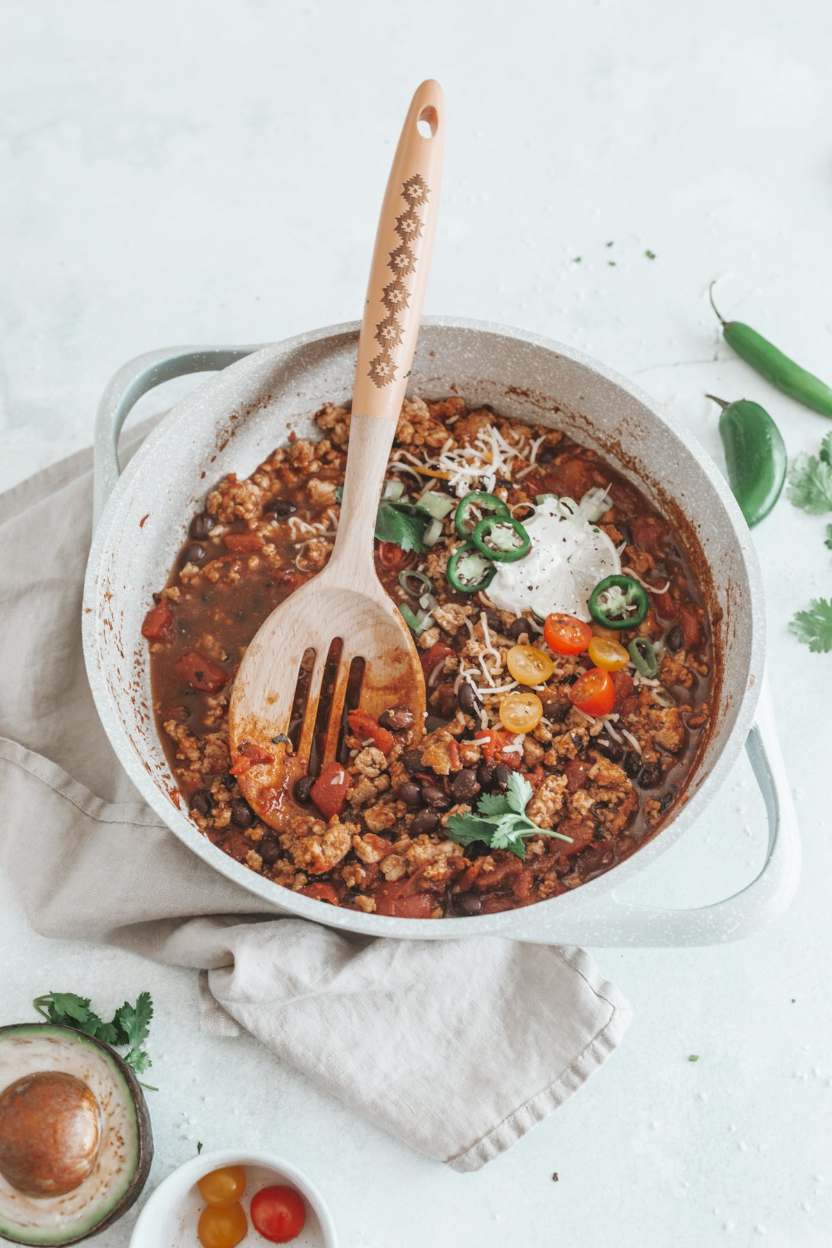 A pan of turkey chili with black beans, tomatoes, coriander and sliced jalapeños